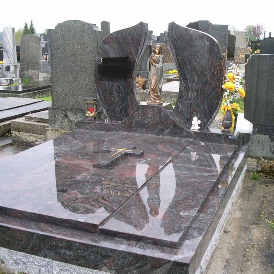 Ein Granitgrabstein mit einem Kreuz, einer Statue einer Frau und einem Blumenvase. Der Grabstein hat eine Inschrift mit Namen und Daten. Der Friedhof hat andere Grabsteine, und einige haben Blumen darauf.