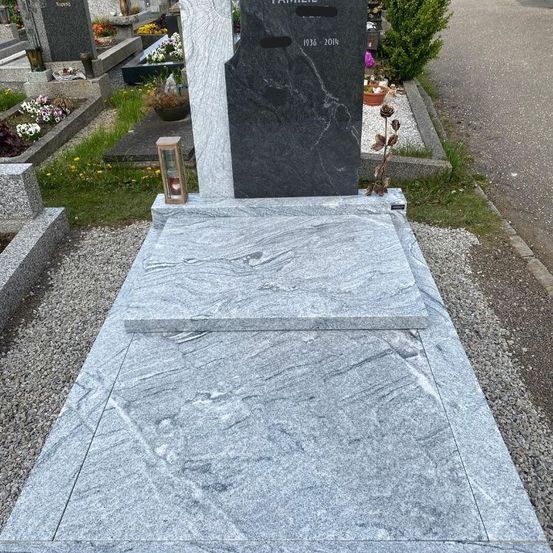 Ein grauer Granitgrabstein für eine Familie steht auf einem Friedhof. Der Grabstein hat die Jahre 1936-2018 eingraviert. Ein Kerzenhalter mit einer Kerze steht auf der linken Seite.