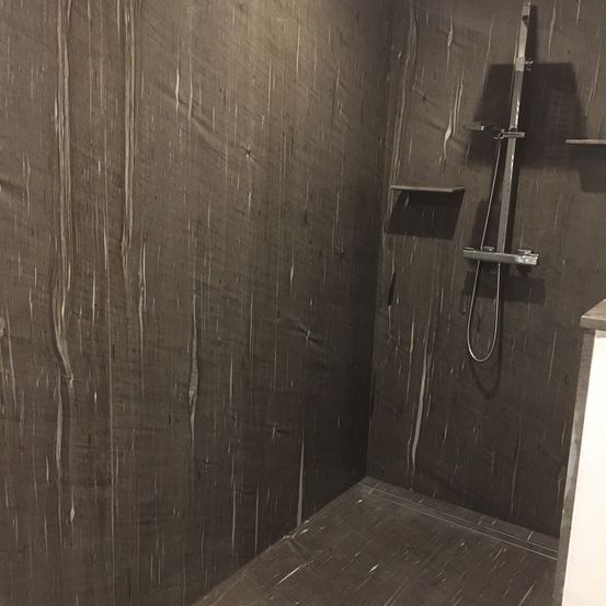 Ein kleiner, dunkler Duschbereich mit Holzwänden und einer silbernen Duschkopf. Es gibt ein Regal und eine kleine Ecke. Der Boden ist nass.