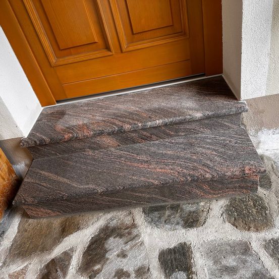 Nahaufnahme von Granitstufen vor einer Holztür. Die Stufen bestehen aus Granit und haben eine grau-braune Farbe.