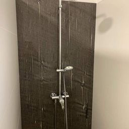 Eine Eckdusche mit Holzwand und Chrom-Duschkopf und -Wasserhahn.