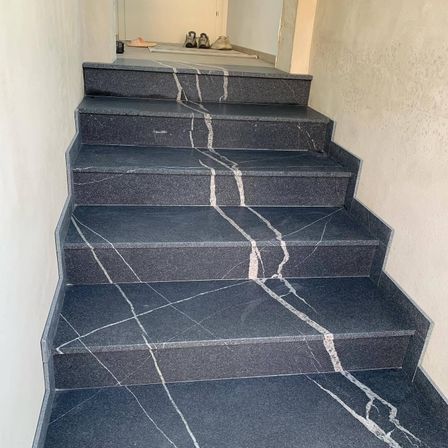 Eine Nahaufnahme einer Marmortreppe mit einem einzigartigen Muster, die zu einem offenen Raum mit Schuhen auf dem Boden führt.