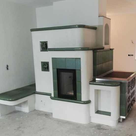 Ein Innenraum mit einem modernen Kamin, grünen Fliesen und einer Bank. Der Raum ist unfertig mit sichtbaren Betonböden und weißen Wänden.