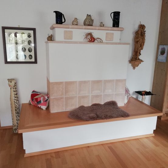 Eine gemütliche Ecke mit einer Holzbank, einem dekorativen Kissen und einem gefliesten Kamin mit verschiedenen Figuren und einem gerahmten Bild an der Wand.
