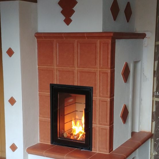 Ein moderner Kamin mit schwarzem Rahmen und orangefarbenen Fliesen, derzeit mit einem warmen Feuer beleuchtet.