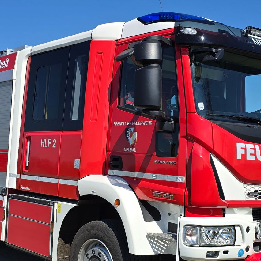 Ein roter und weißer Feuerwehrwagen steht auf einer Straße mit klarem blauem Himmel im Hintergrund. Der Wagen trägt die Aufschrift 'FEUERWEHR IVECO' auf der Vorderseite und ein Nummernschild mit der Aufschrift 'FW 371 MI'.