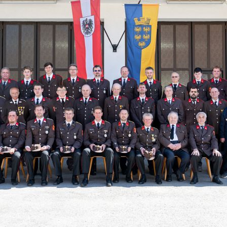 Eine Gruppe von Militärangehörigen in Uniform posiert für ein Foto vor einem Gebäude mit Fahnen an der Wand.