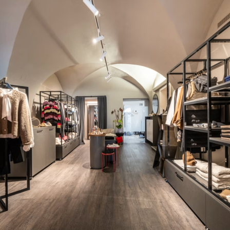 Das Innere eines Boutique-Kleidunggeschäfts mit Holzböden, gewölbter Decke und modernen Regalen. Kleidung ist ordentlich auf den Gestellen angeordnet.