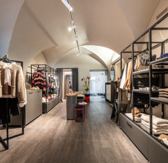 Das Innere eines Boutique-Kleidunggeschäfts mit Holzböden, gewölbter Decke und modernen Regalen. Kleidung ist ordentlich auf den Gestellen angeordnet.