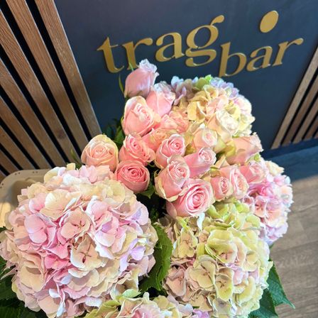 Ein Nahaufnahme eines großen Straußes aus rosa und weißen Rosen und Hortensien, vor einem Schild für 'tragbar' angeordnet.