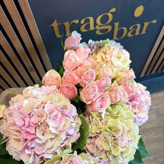 Ein Nahaufnahme eines großen Straußes aus rosa und weißen Rosen und Hortensien, vor einem Schild für 'tragbar' angeordnet.