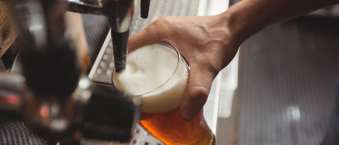 Eine Person zapft Bier von einem Zapfhahn in ein Glas in einer Bar ab.