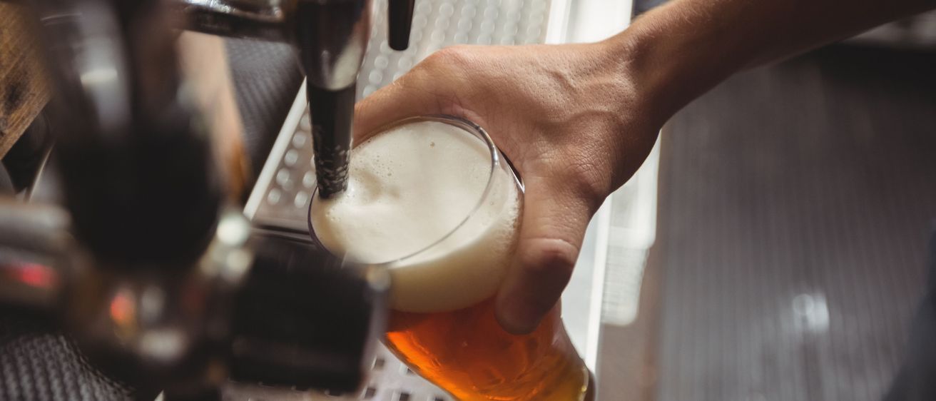 Eine Person zapft Bier von einem Zapfhahn in ein Glas in einer Bar ab.