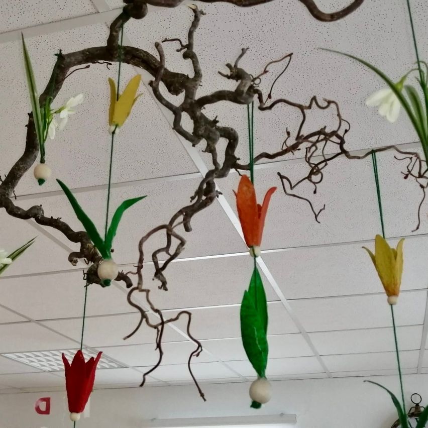 Eine Decke, verziert mit einer Sammlung von Zweigen, die künstliche Blumen tragen. Jeder Zweig hängt mit leuchtenden Tulpen in verschiedenen Farben, einschließlich weiß, gelb und rot, an grünen Blättern von der Decke herab.