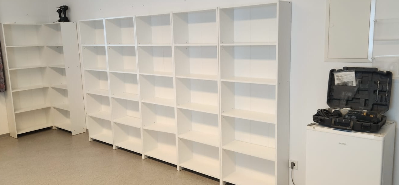 Eine Reihe weißer Regale an einer weißen Wand, jedes Regal hat mehrere Abteile, und der Boden ist mit einem hellen Material bedeckt.