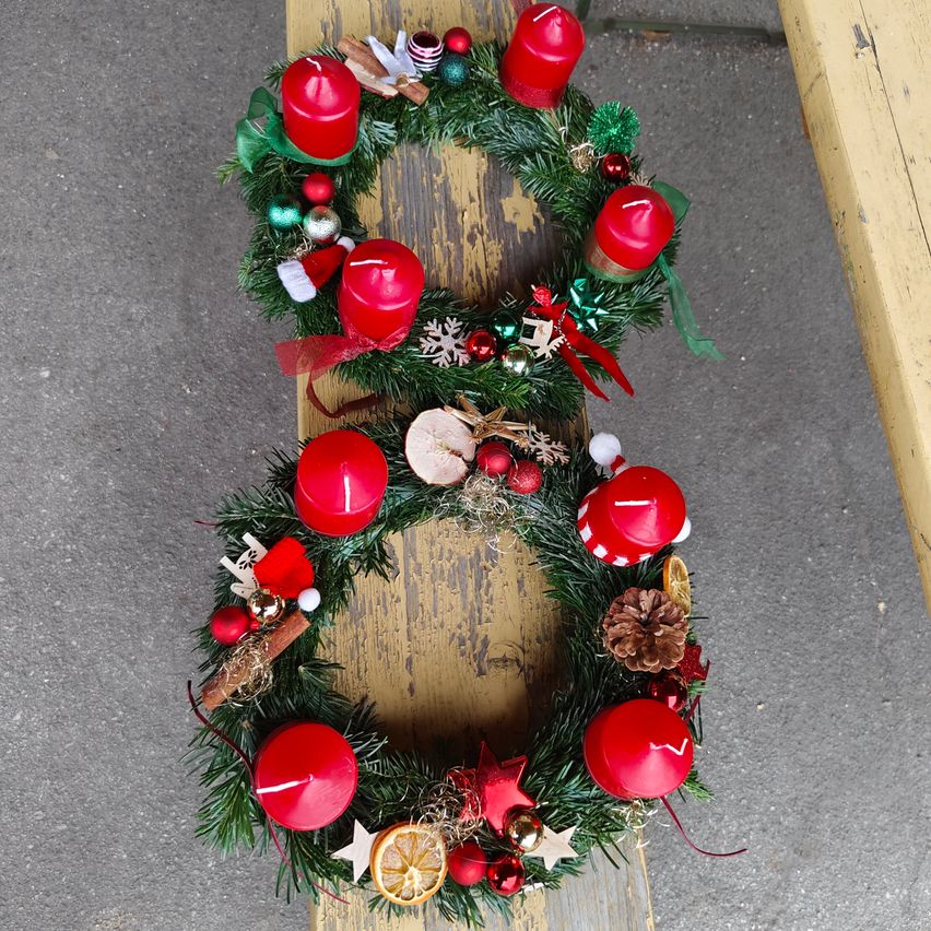 Ein Kranz mit acht roten Kerzen, grünem Laub, Ornamenten und Sternen auf einer Holzoberfläche.