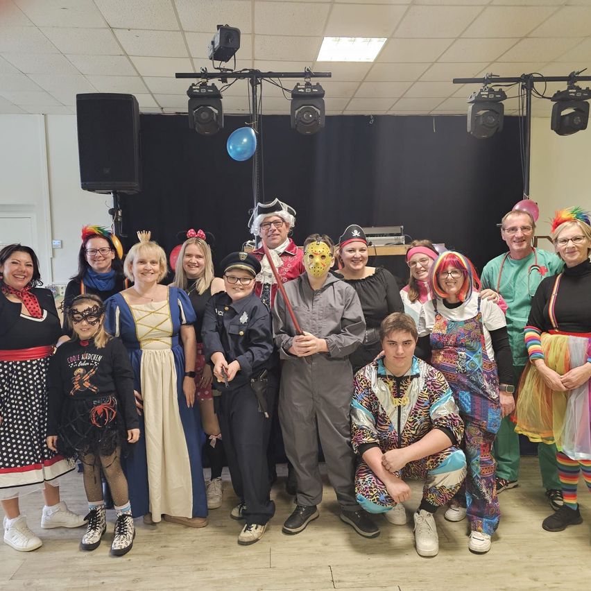 Eine Gruppe von Menschen in Kostümen posiert für ein Foto in einem Raum mit Luftballons und Lautsprechern.