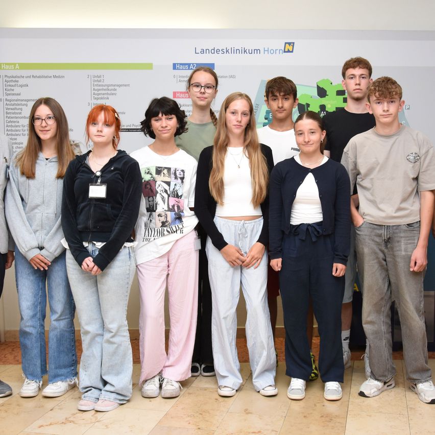 Eine Gruppe junger Personen, wahrscheinlich Medizinpraktikanten, steht zusammen vor einer Krankenhauskarte. Die Karte ist mit Bereichen wie Haus A und Haus A2 beschriftet.