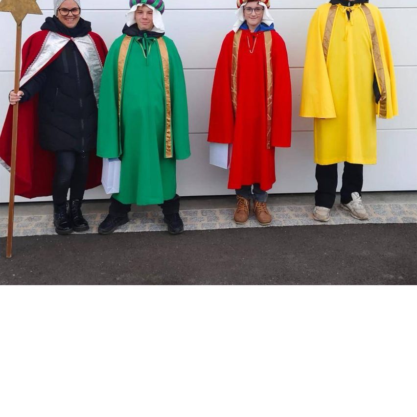 Vier Menschen sind in Kostümen gekleidet, möglicherweise für ein Theaterstück. Die Person auf der linken Seite hält einen goldenen Stab. Die Person auf der rechten Seite trägt einen gelben Umhang.