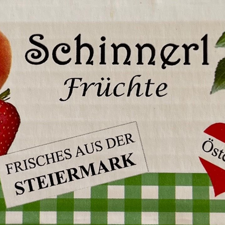 Ein weißer Hintergrund mit grün-weiß kariertem Tuch zeigt einen Markennamen 'Schinnerl Friichte'. Ein Bild einer Erdbeere und einer Orange ist links platziert, mit einem roten Herzsymbol rechts. Ein weißer Aufkleber mit dem Text 'FRICHES AUS DER STEIERMARK' ist links.