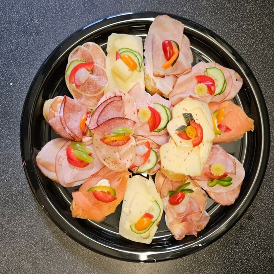 Ein schwarzer Teller gefüllt mit einer Auswahl an Sandwiches, jedes belegt mit bunten Gemüsen und Fleisch, kunstvoll arrangiert.