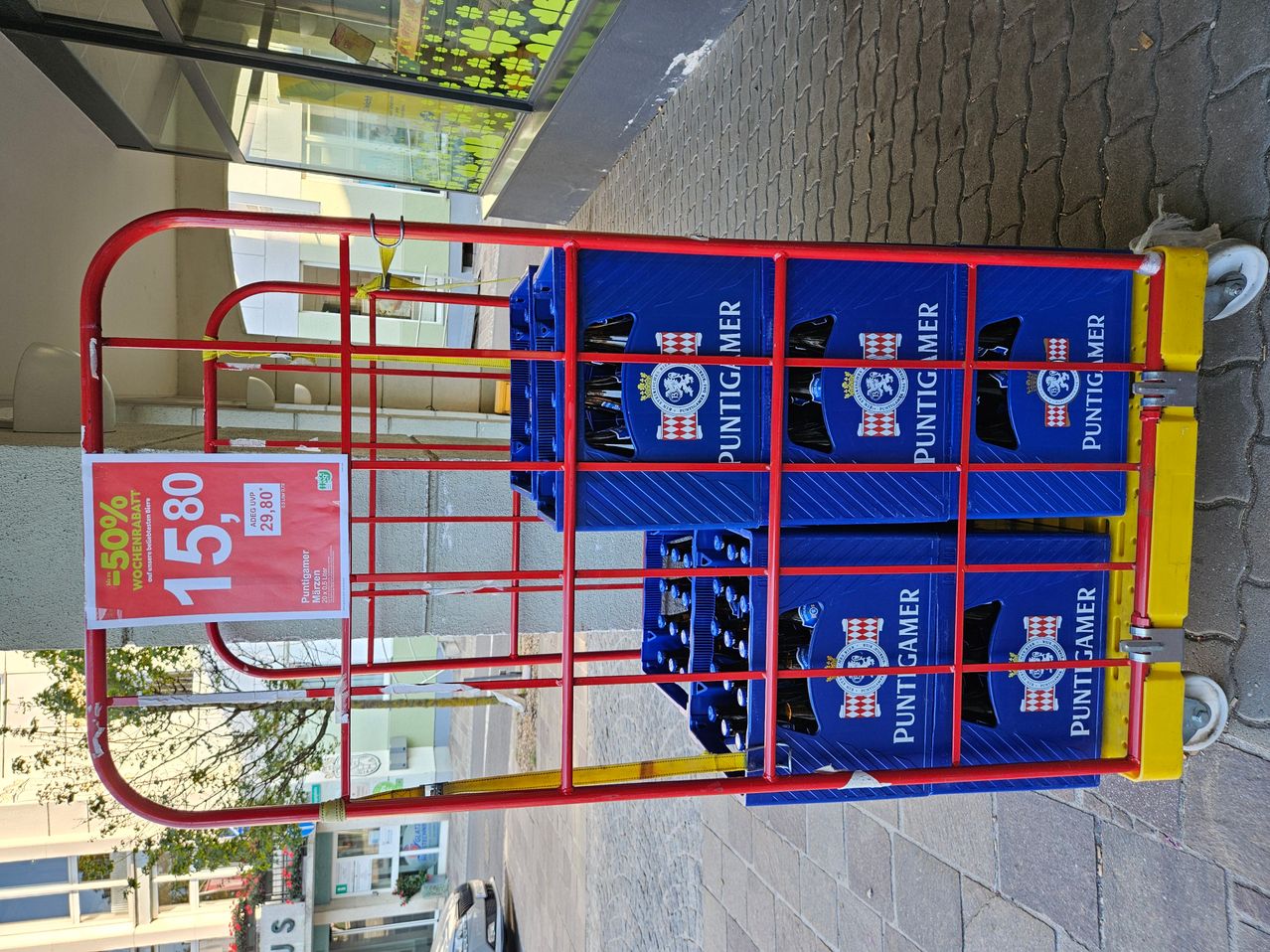 A red cart with blue crates stacked on it, each containing Puntigamer beer bottles. A red sign with the price of 15.80 euros is visible.
