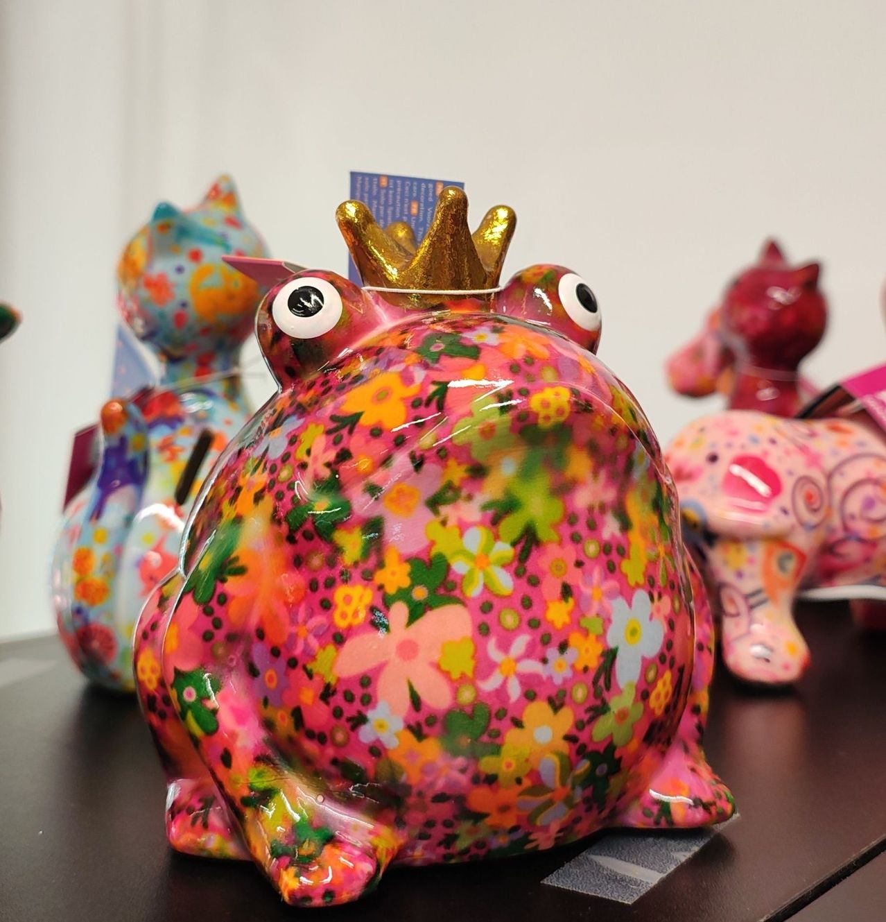 Eine farbenfrohe Froschfigur mit Krone und Blumenmuster, begleitet von anderen bunten Tierfiguren auf einem Tisch.