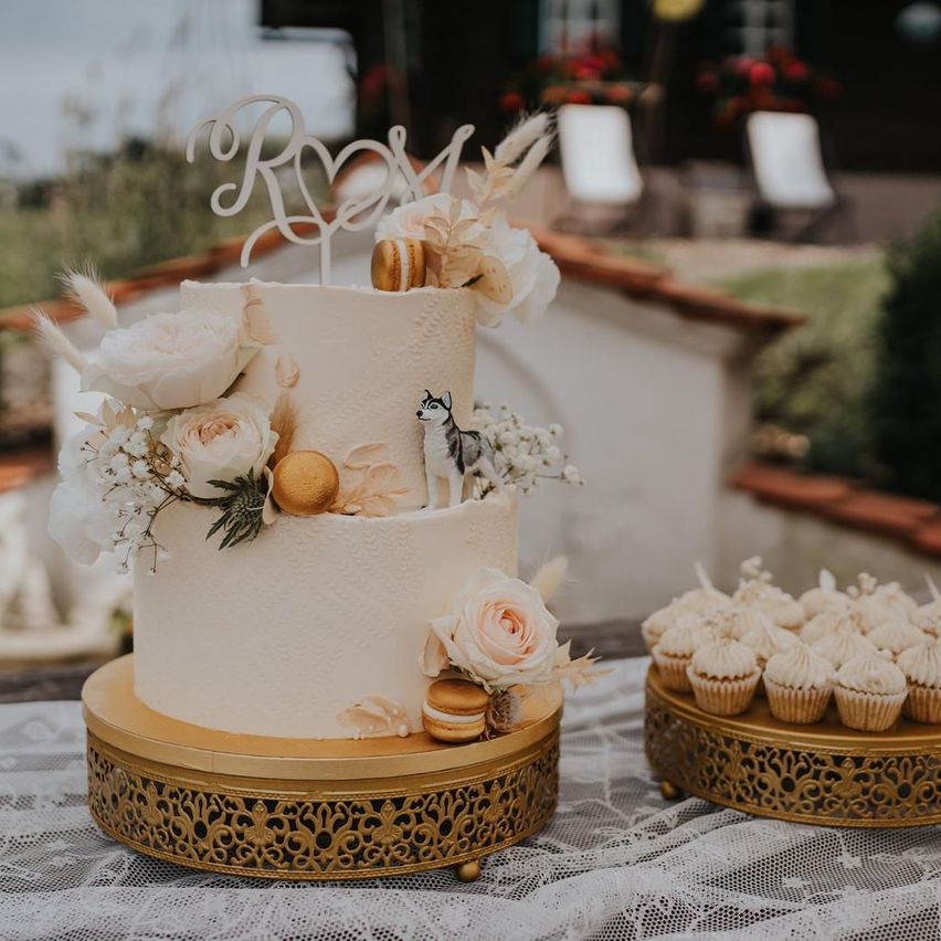 A three-tiered wedding cake with white and gold decorations, including a husky figurine, on a gold stand.