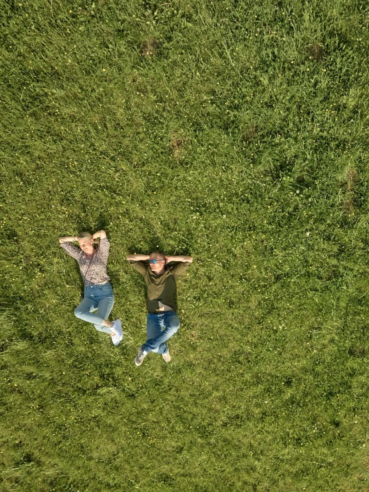 Zwei Menschen liegen auf einem Grasfeld, einer trägt eine Sonnenbrille und ein Armband, der andere ein grünes Shirt.