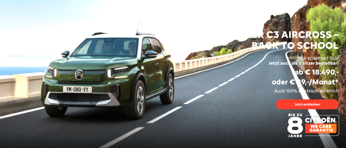 Ein grüner SUV fährt auf einer Straße mit weißen Markierungen, begleitet von einer Steinmauer und Grün.