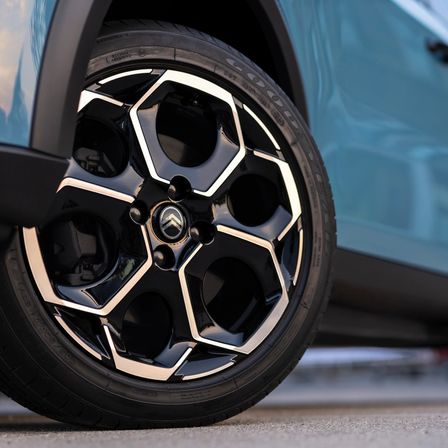 Nahaufnahme eines Autoreifens mit schwarzem Reifen und silbernen Felgen mit sechseckigem Muster. Das Fahrzeug ist hellblau.