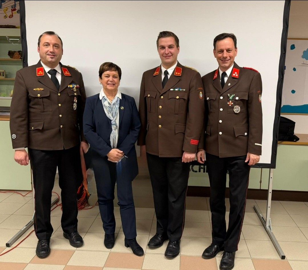 Vier Personen in Uniform posieren für ein Foto; eine Frau in einem blauen Anzug steht zwischen zwei Männern in Militäruniform.