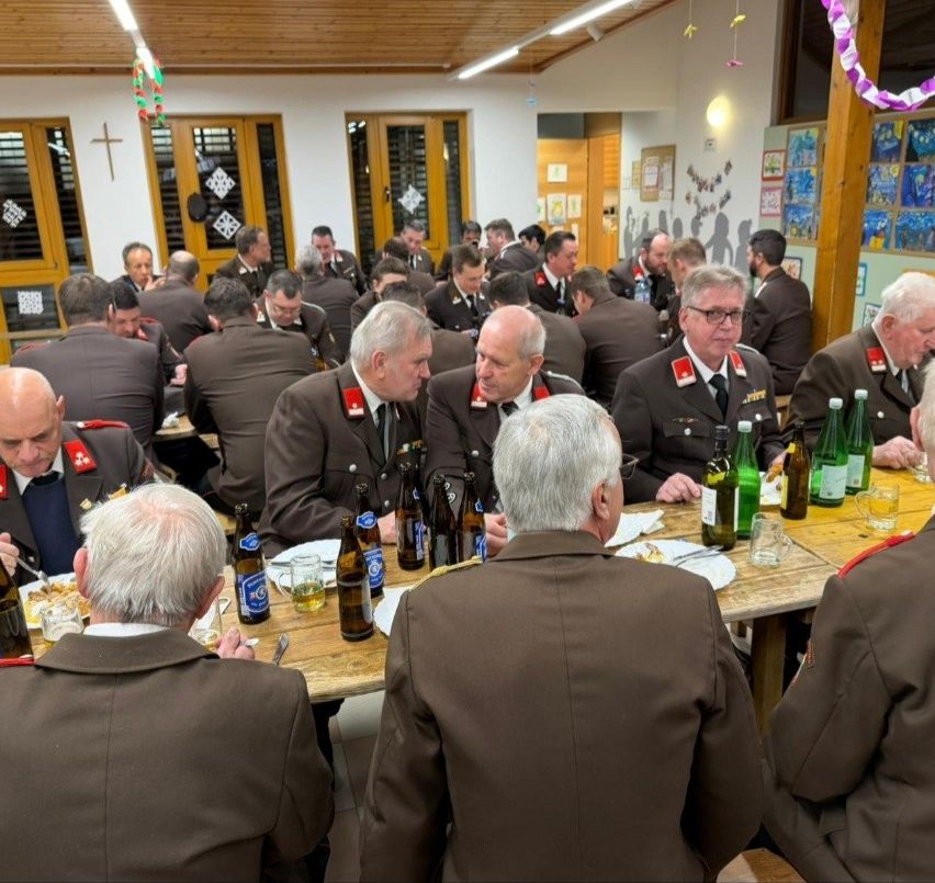 Eine Gruppe von Männern in Uniform sitzt um einen Tisch für eine Mahlzeit, mit Flaschen und Gläsern auf dem Tisch und Bildern an der Wand.