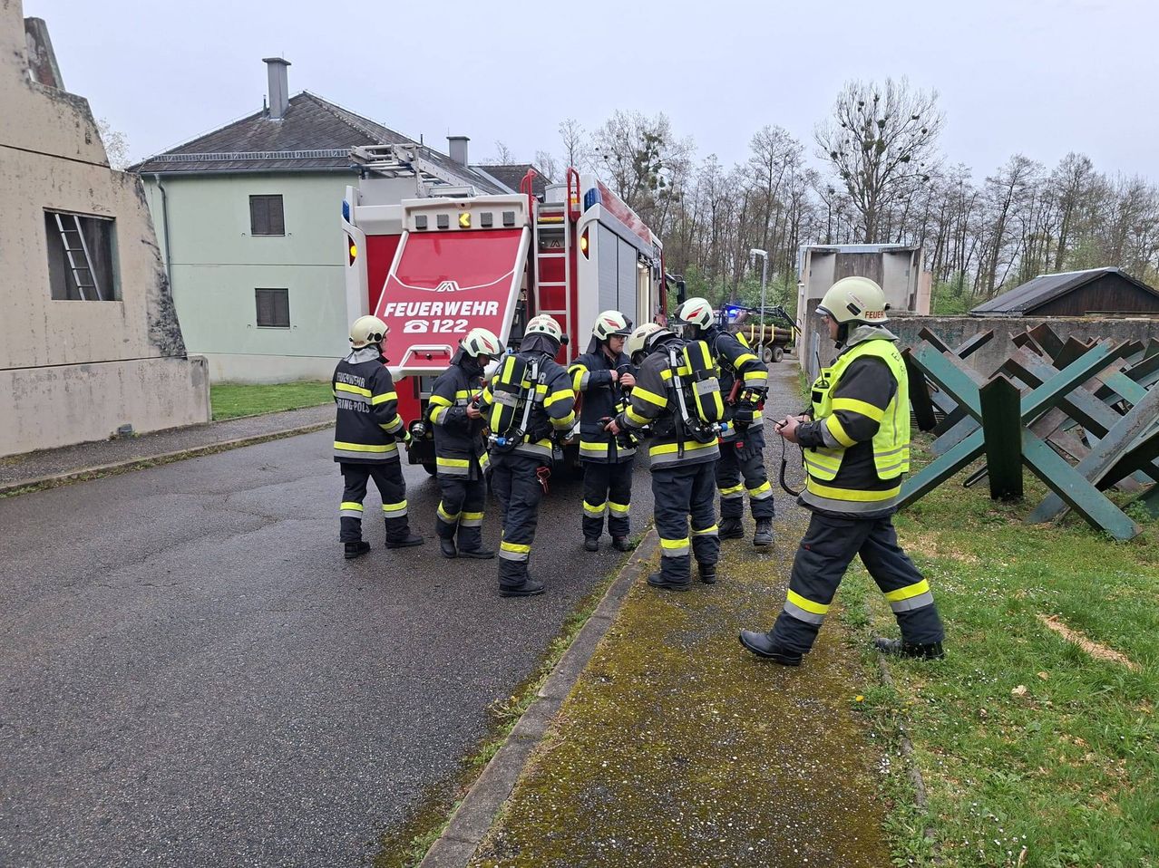 A group of firefighters in uniforms with helmets and protective gear gather around a fire truck. The truck has the text 'Feuerwehr' and the number 122 on the side.
