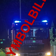 Ein Feuerwehrauto mit eingeschalteten Blaulicht, in einem dunklen Bereich in der Nacht geparkt. Das Wort 'FEUERWEHR' ist vorne sichtbar.