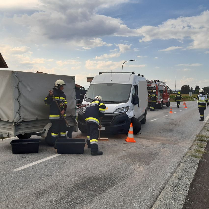 Feuerwehrleute reinigen eine Verschüttung auf der Straße mit einem weißen Lieferwagen und einem Anhänger in der Nähe.