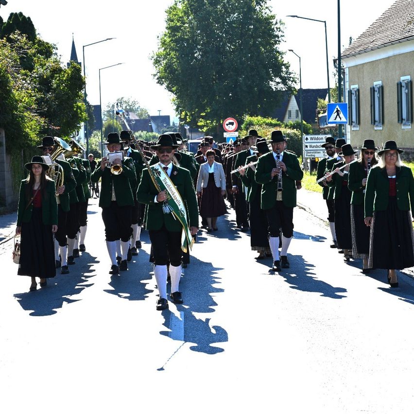 Eine Gruppe von Menschen in grünen Uniformen marschiert die Straße entlang und trägt Musikinstrumente.