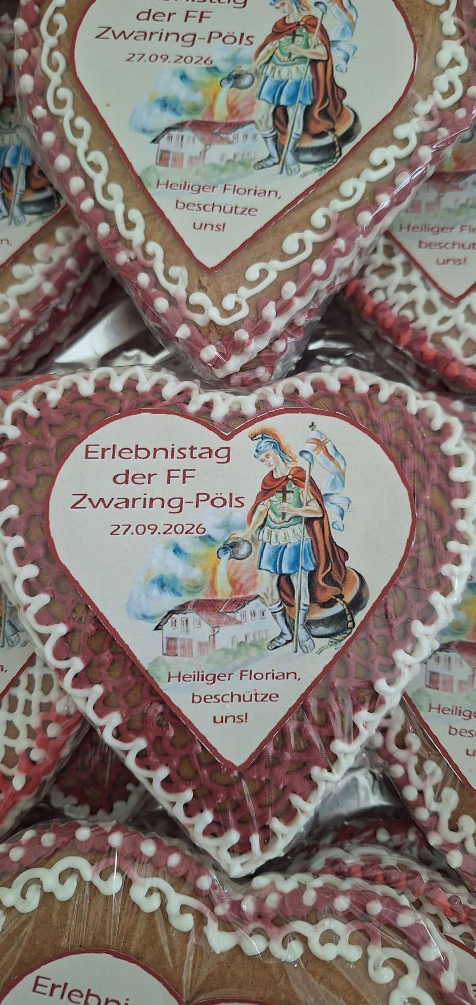 Ein Stapel herzförmiger Kekse mit weißem Zuckerguss-Design, das eine Illustration eines Ritters und den Text 'Erlebnistag der FF Zwaring-Pöls 27.09.2026' zeigt.