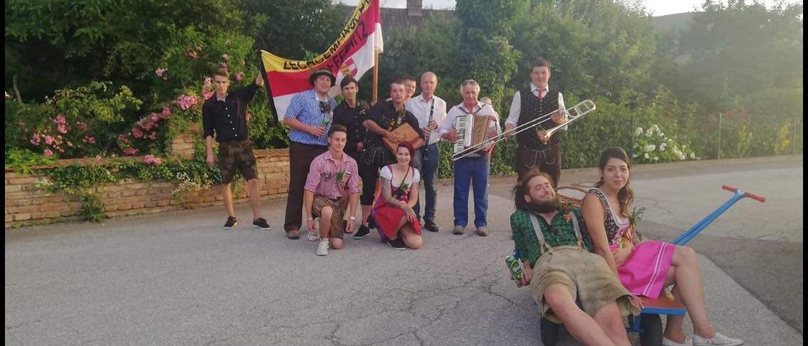 Eine Gruppe von Menschen in traditioneller bayerischer Kleidung posiert für ein Foto mit Musikinstrumenten und einer Flagge.