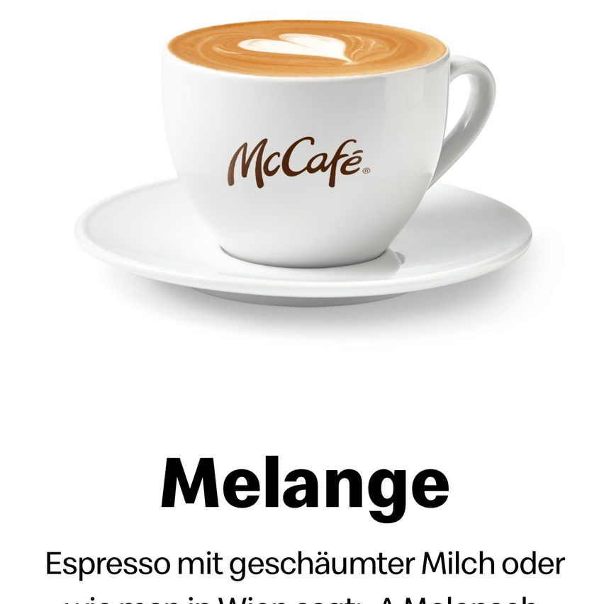 Eine weiße Kaffeetasse mit brauner Latte-Kunst steht auf einer Untertasse. Die Tasse hat das Wort 'McCafé' darauf geschrieben. Darunter steht das Wort 'Melange' und eine Beschreibung davon.