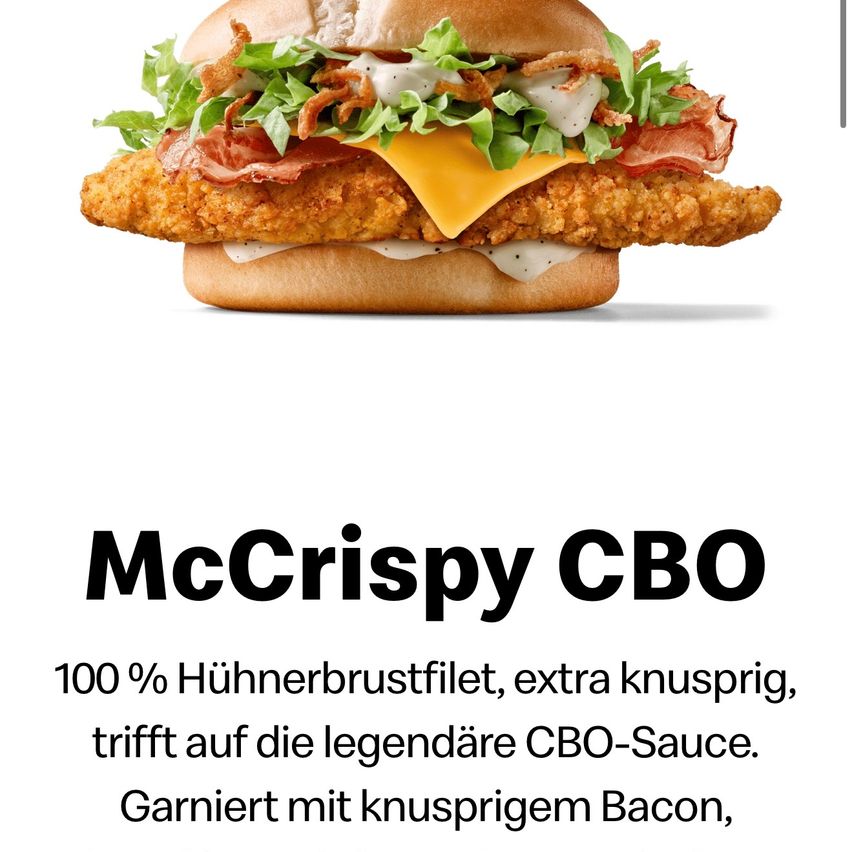 Ein Nahaufnahme eines knusprigen Hähnchenburgers mit Salat, Käse, Speck und einer cremigen Sauce, gekennzeichnet als 'McCrispy CBO'. Der Burger ist auf weißem Hintergrund mit einem fettgedruckten schwarzen Textüberlagerung.