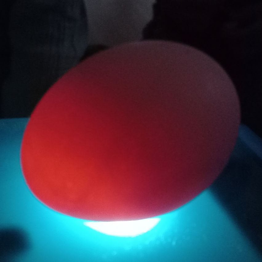 Eine leuchtend rote Kugel wird von unten von einem blauen Licht beleuchtet, möglicherweise in einem dunklen Raum.