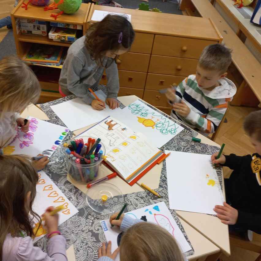 Eine Gruppe junger Kinder sitzt um einen Tisch herum und malt mit Markern auf Papier.