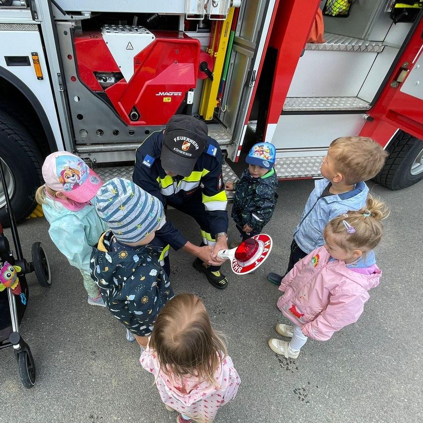 Ein Feuerwehrmann zeigt einer Gruppe von Kindern eine blinkende Lampe. Die Kinder schauen neugierig auf die Lampe.