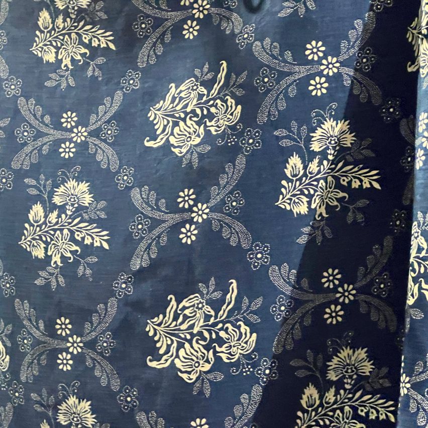 Ein Nahaufnahme von blauem Stoff mit komplizierten goldenen Blumenmustern. Das Design zeigt zarte Blumen und Blätter und erzeugt eine visuell ansprechende Textur.