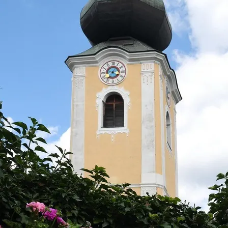 Ein Turm mit einer Uhr, umgeben von Bäumen. Die Uhr zeigt die Zeit 10:10 an.