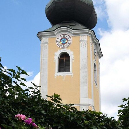 Ein Turm mit einer Uhr, umgeben von Bäumen. Die Uhr zeigt die Zeit 10:10 an.