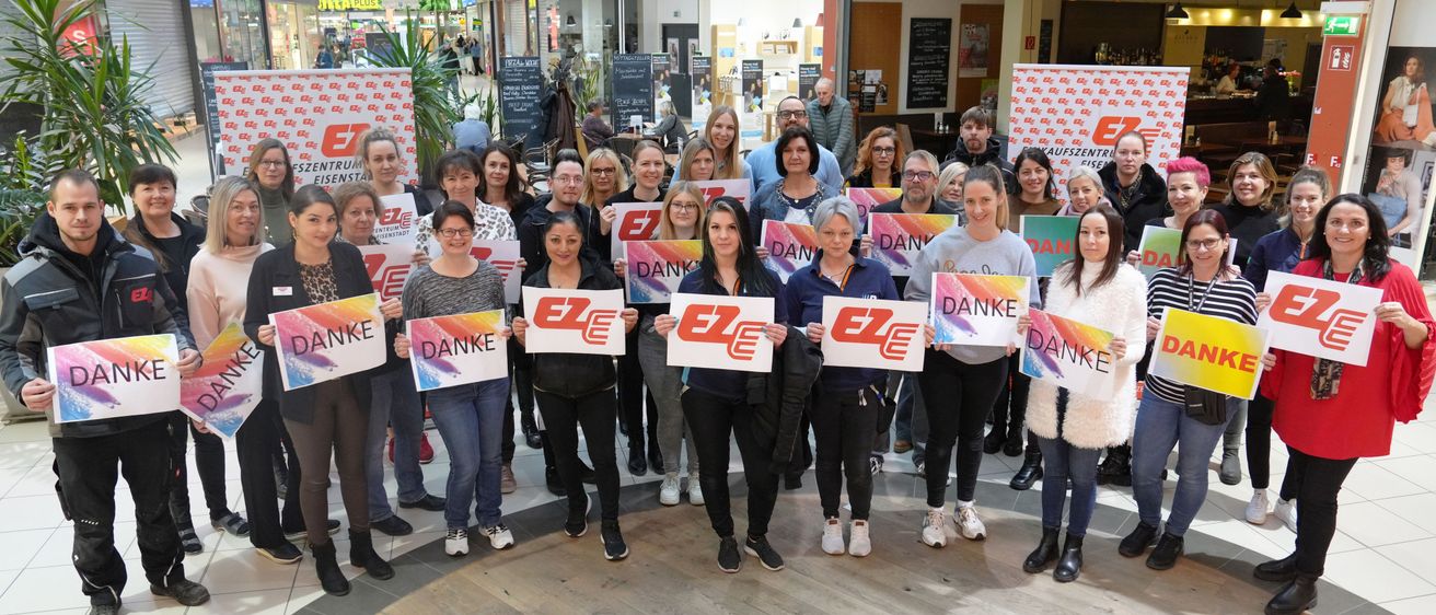 Gruppe von Menschen, die weiße Schilder mit roten Buchstaben halten, die Danke sagen. Sie stehen in einem Einkaufszentrum.