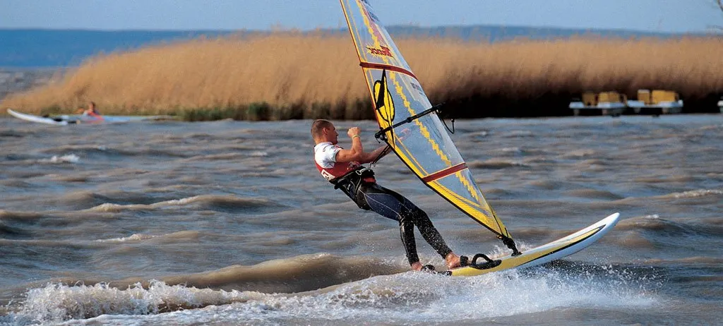 Ein Mann windsurft auf einer welligen See, hält mit einer Hand das Segel fest und balanciert auf einem Board.