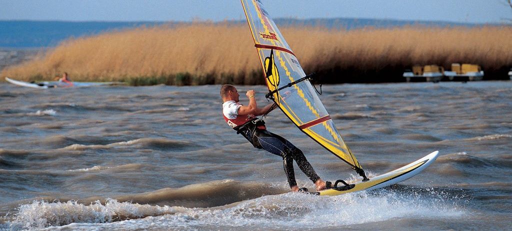 Ein Mann windsurft auf einer welligen See, hält mit einer Hand das Segel fest und balanciert auf einem Board.